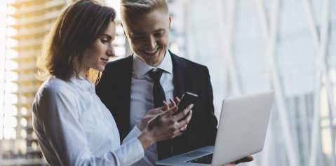 Happy smiling businessman and businesswoman using laptop and smartphone while working on new project, two young professional employers working on portable computer and discussing project of consctrustions outdoors, flare light